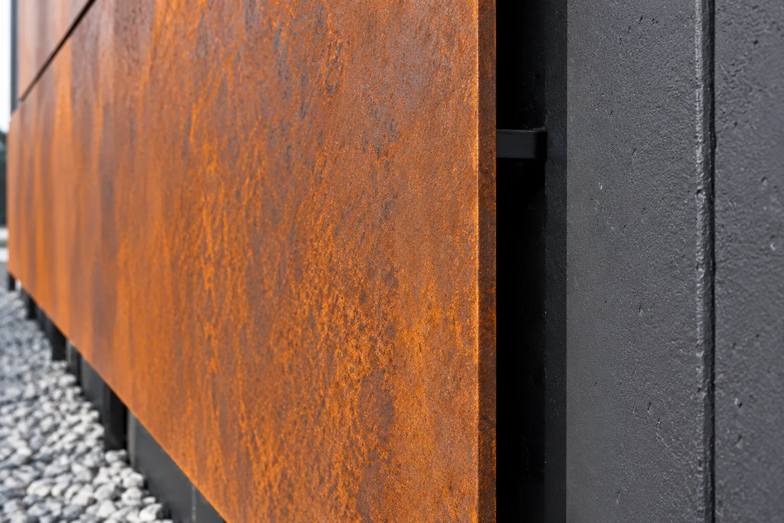 Edge of an orange-brown steel panel standing off a dark wall, with a dark air gap along the edge
