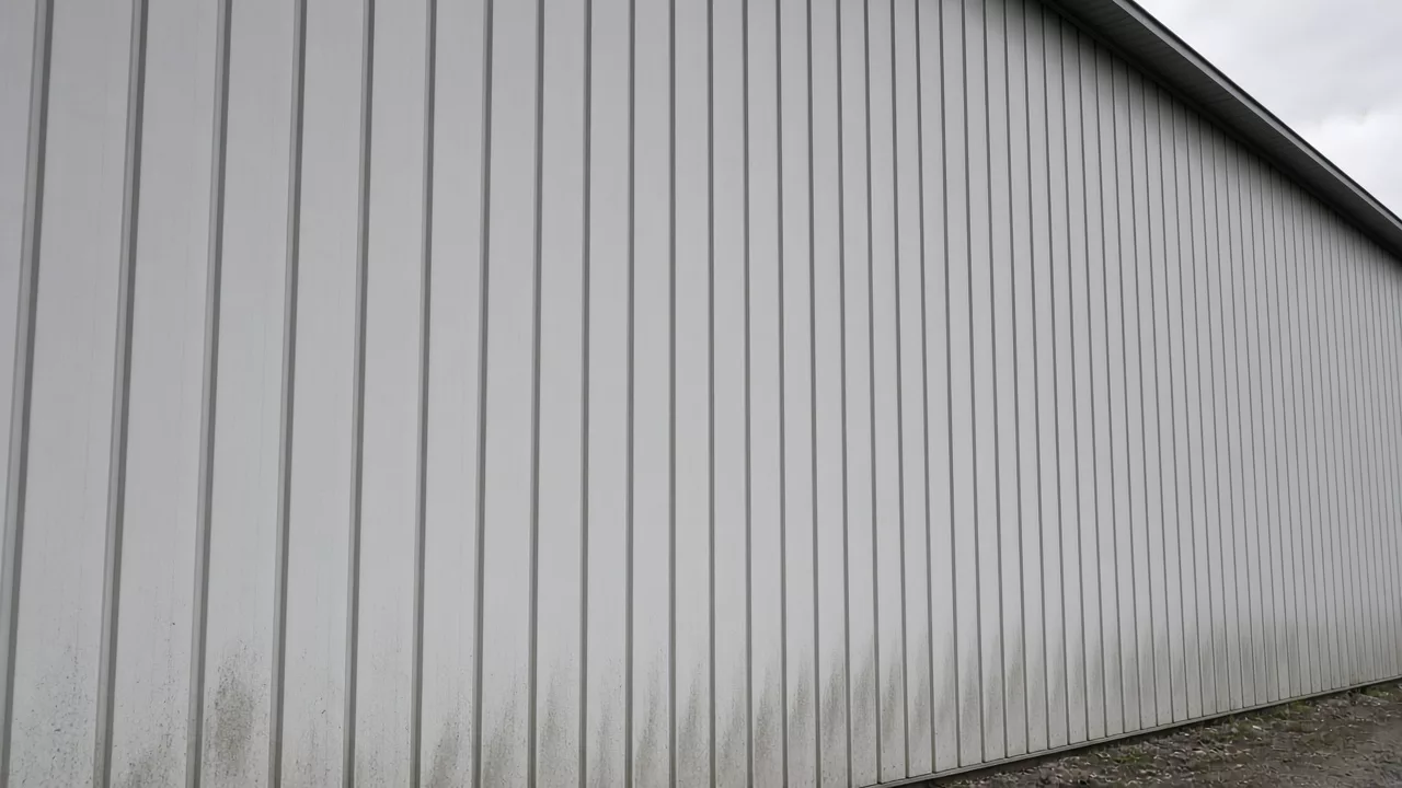 Ribbed pale metal wall with dirt along the bottom edge under an overcast sky.