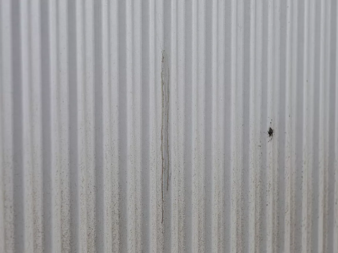 Close view of ribbed pale metal with dust, a vertical streak, and a small dark speck.